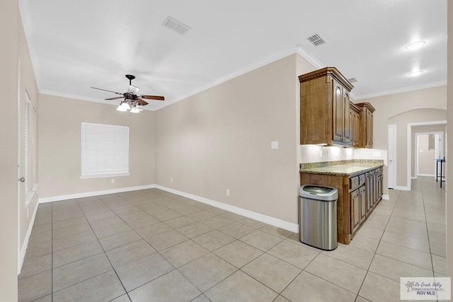 kitchen with light stone counters, arched walkways, light tile patterned floors, visible vents, and ornamental molding