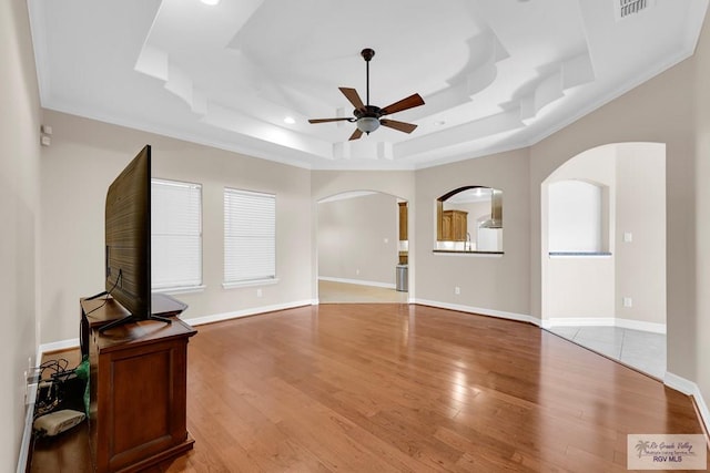 living area with baseboards, arched walkways, a raised ceiling, a ceiling fan, and light wood-style floors