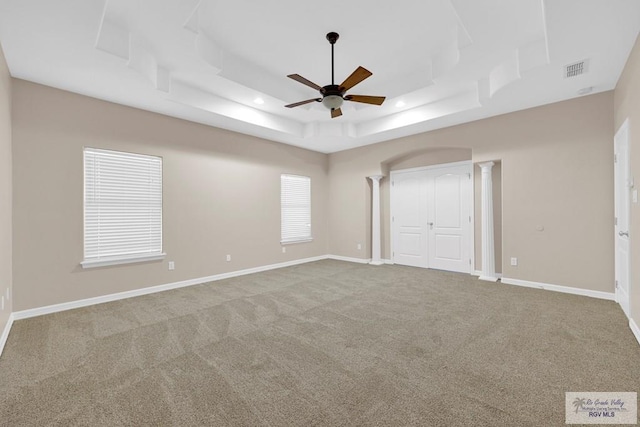 unfurnished bedroom with a tray ceiling, carpet, visible vents, baseboards, and ornate columns