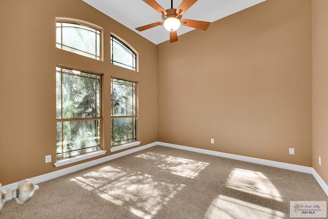 carpeted spare room with ceiling fan, a towering ceiling, and baseboards