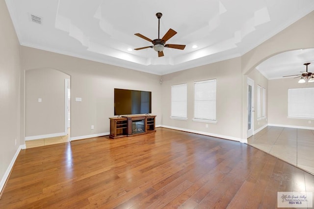 unfurnished living room with arched walkways, visible vents, ceiling fan, and a tray ceiling