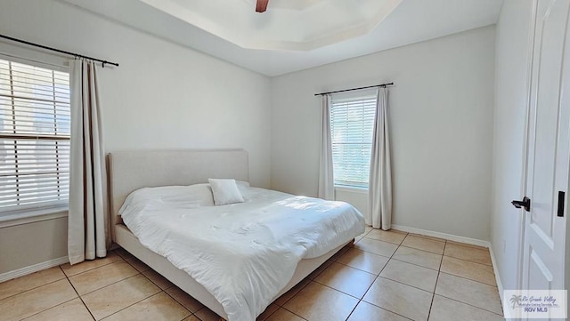 bedroom with light tile patterned floors, ceiling fan, a tray ceiling, and baseboards