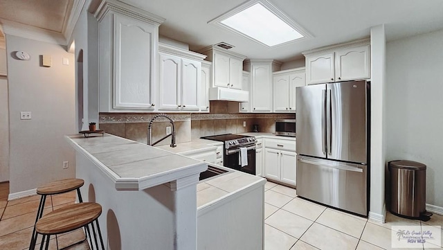 kitchen featuring under cabinet range hood, stainless steel appliances, a peninsula, a kitchen breakfast bar, and white cabinets