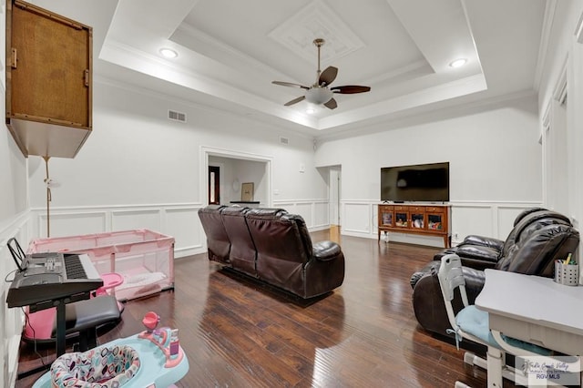 living room featuring a raised ceiling, visible vents, a ceiling fan, and ornamental molding