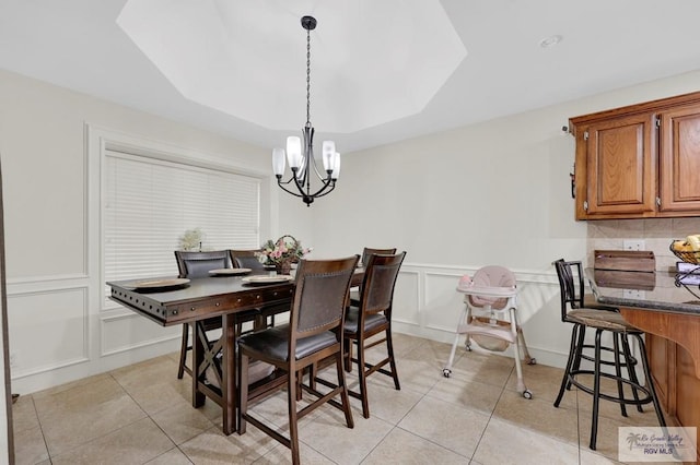 dining room with a wainscoted wall, a chandelier, light tile patterned floors, and a decorative wall