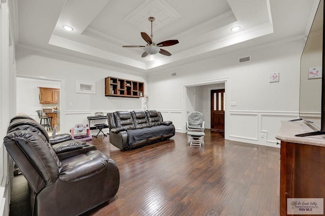 living area featuring dark wood-style flooring, a ceiling fan, a raised ceiling, ornamental molding, and visible vents