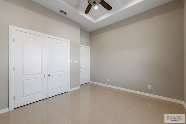 unfurnished bedroom with a closet, visible vents, baseboards, a ceiling fan, and a tray ceiling