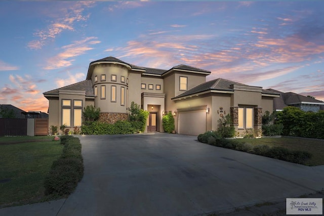 view of front of house with stucco siding, fence, stone siding, driveway, and a garage