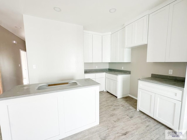 kitchen with light hardwood / wood-style flooring, white cabinets, and an island with sink