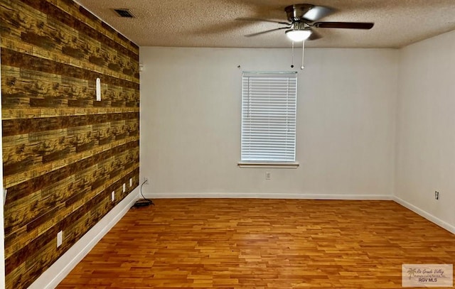 unfurnished room featuring ceiling fan, wood walls, a textured ceiling, and light hardwood / wood-style flooring