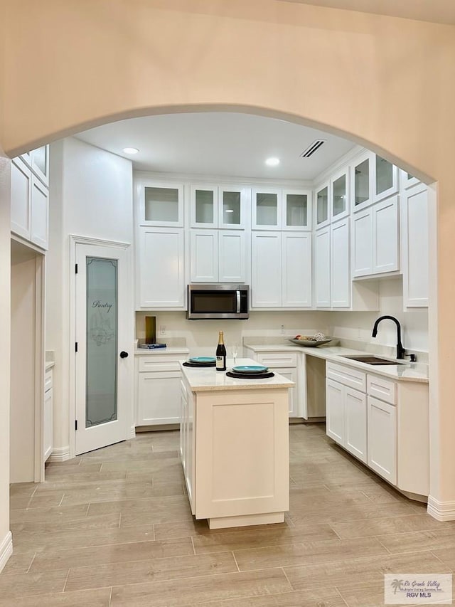 1521 Stirrup Cir, San Benito, TX 78586 - kitchen featuring a sink, stainless steel microwave, arched walkways, white cabinets, and recessed lighting