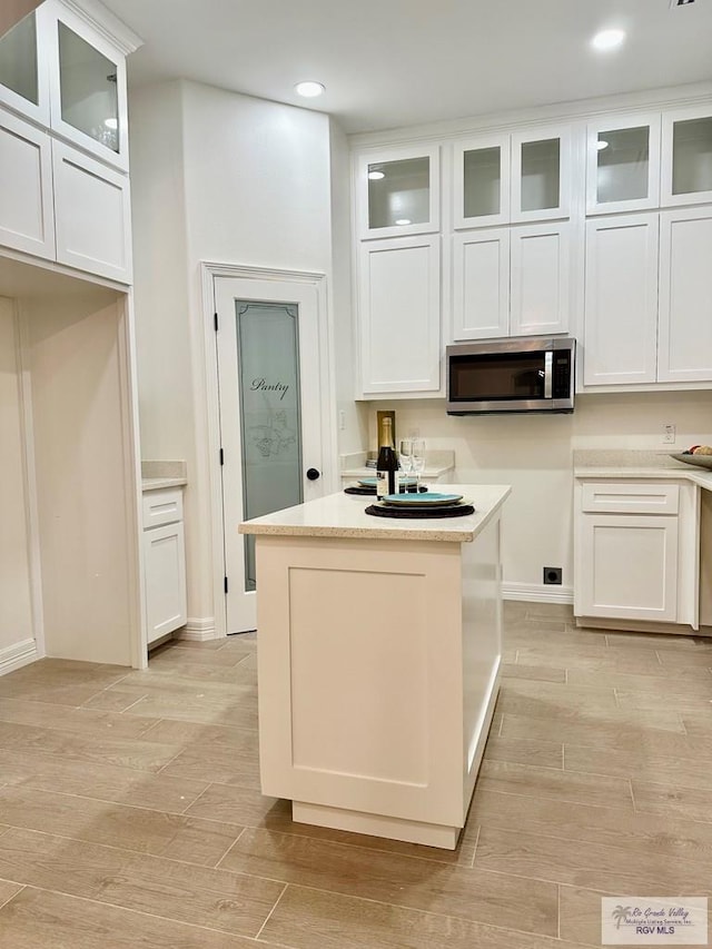1521 Stirrup Cir, San Benito, TX 78586 - kitchen featuring stainless steel microwave, white cabinetry, light wood finished floors, glass insert cabinets, and recessed lighting