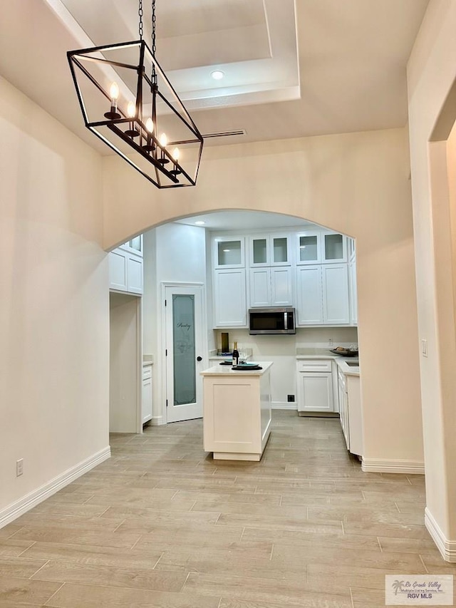 1521 Stirrup Cir, San Benito, TX 78586 - kitchen featuring arched walkways, stainless steel microwave, light wood finished floors, glass insert cabinets, and a raised ceiling