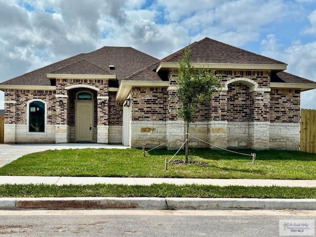 1521 Stirrup Cir, San Benito, TX 78586 - french provincial home with a shingled roof, brick siding, an attached garage, and stone siding