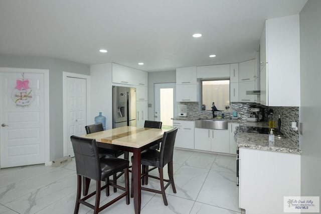 kitchen with sink, light stone counters, stainless steel refrigerator with ice dispenser, backsplash, and white cabinets