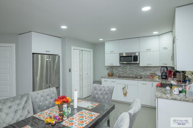 kitchen featuring decorative backsplash, white cabinetry, light stone counters, and appliances with stainless steel finishes