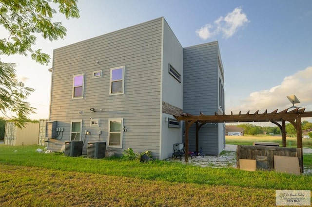 rear view of house featuring a pergola, cooling unit, and a lawn