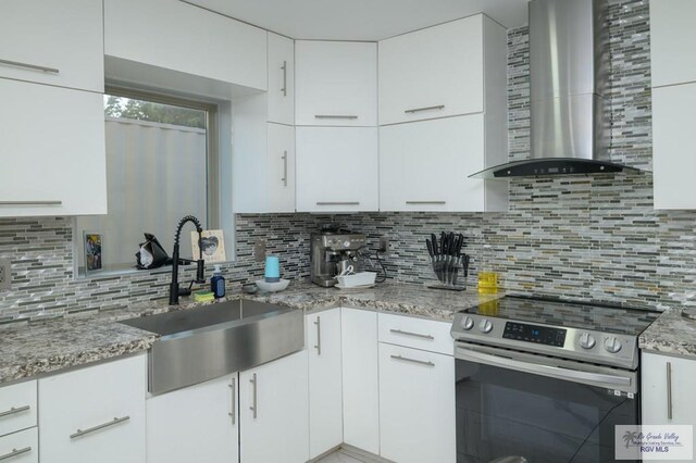 kitchen with wall chimney range hood, sink, electric range, tasteful backsplash, and white cabinetry