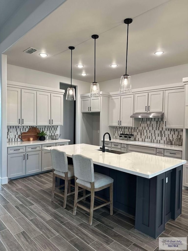 3518 Treasure Hills Blvd, Harlingen, TX 78550 - kitchen with tasteful backsplash, wood tiled floors, under cabinet range hood, a kitchen island with sink, and pendant lighting