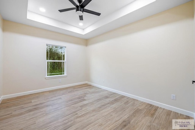 unfurnished room with ceiling fan, light hardwood / wood-style floors, and a tray ceiling