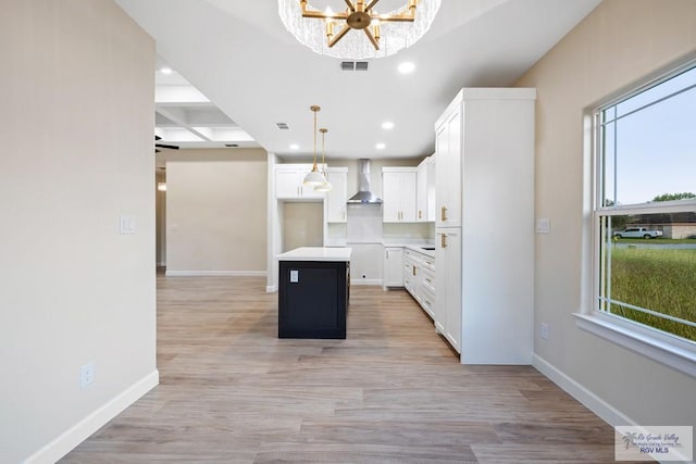 kitchen featuring a center island, white cabinets, hanging light fixtures, and wall chimney range hood