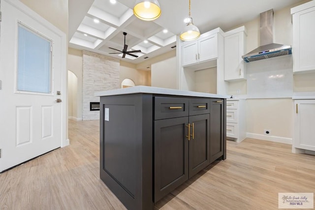 kitchen with coffered ceiling, wall chimney range hood, white cabinets, light hardwood / wood-style floors, and hanging light fixtures