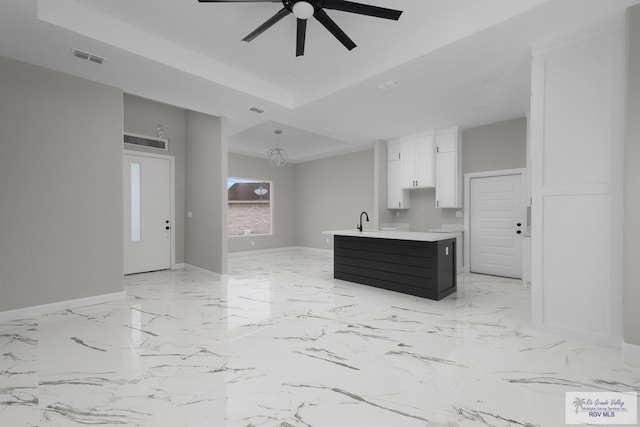 kitchen with sink, a center island, a tray ceiling, ceiling fan, and white cabinets