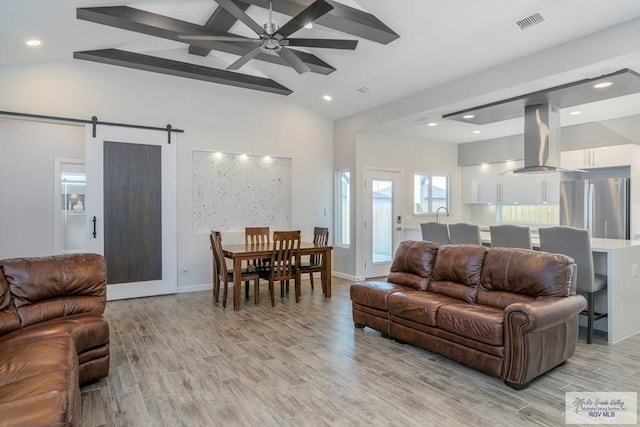 living room featuring vaulted ceiling with beams, a barn door, and light hardwood / wood-style flooring