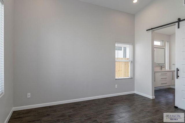 unfurnished bedroom featuring a barn door, dark wood-type flooring, and connected bathroom