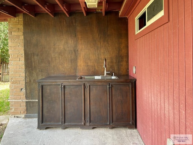 bar featuring dark brown cabinets, wood walls, and sink