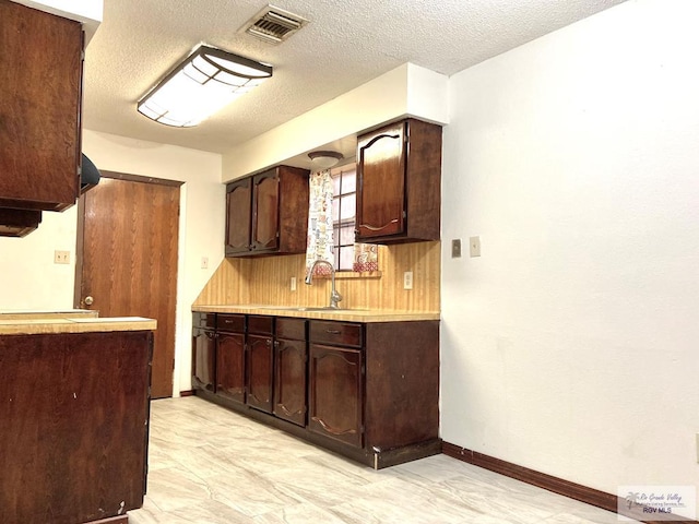 kitchen with dark brown cabinetry, sink, and a textured ceiling