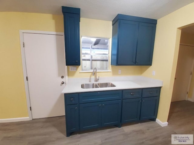 608 W Polk St, Harlingen, TX 78550 - kitchen with blue cabinetry, a sink, light countertops, and light wood-style floors