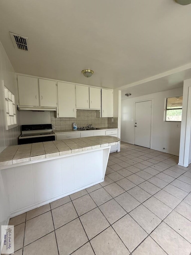1206 S C St, Harlingen, TX 78550 - kitchen featuring electric range oven, tile counters, under cabinet range hood, decorative backsplash, and light tile patterned floors