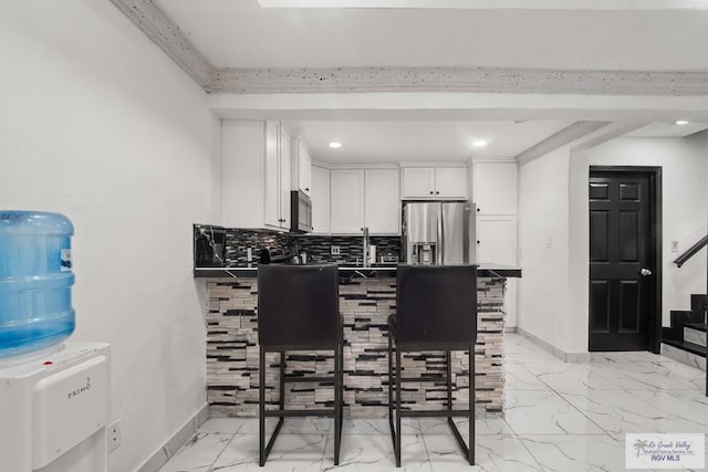 kitchen with kitchen peninsula, appliances with stainless steel finishes, backsplash, a breakfast bar, and white cabinetry