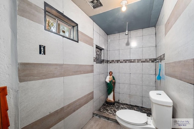 bathroom with toilet, tile walls, and a tile shower