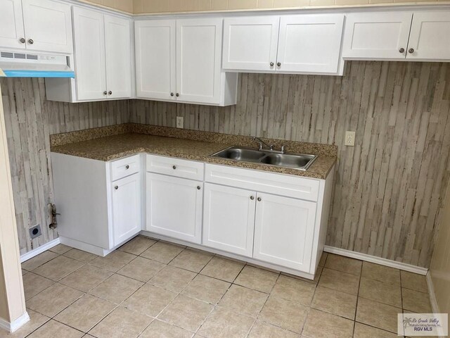 kitchen featuring white cabinets, wooden walls, and sink