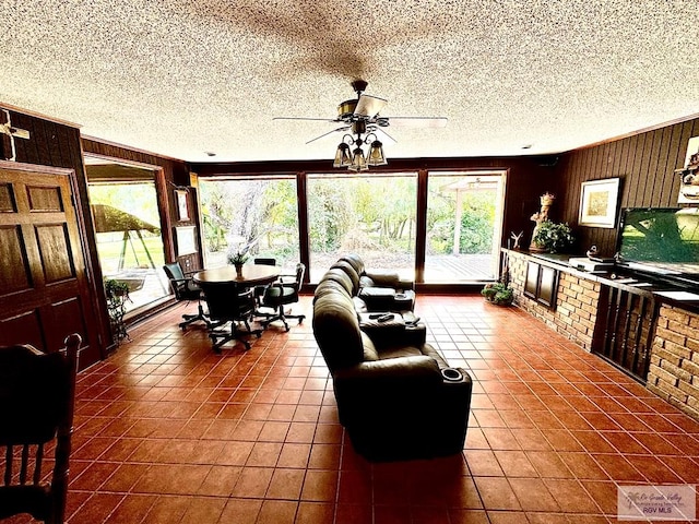 tiled living room featuring ceiling fan, wooden walls, and a textured ceiling