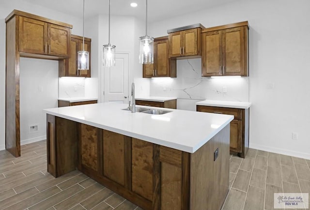 kitchen featuring pendant lighting, sink, an island with sink, tasteful backsplash, and wood-type flooring