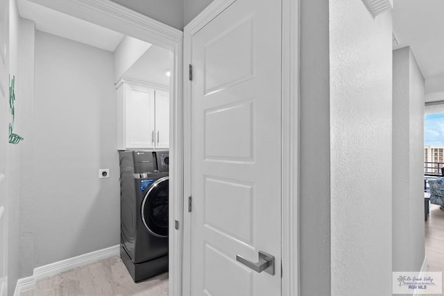 clothes washing area featuring baseboards, washer / clothes dryer, cabinet space, and a textured wall