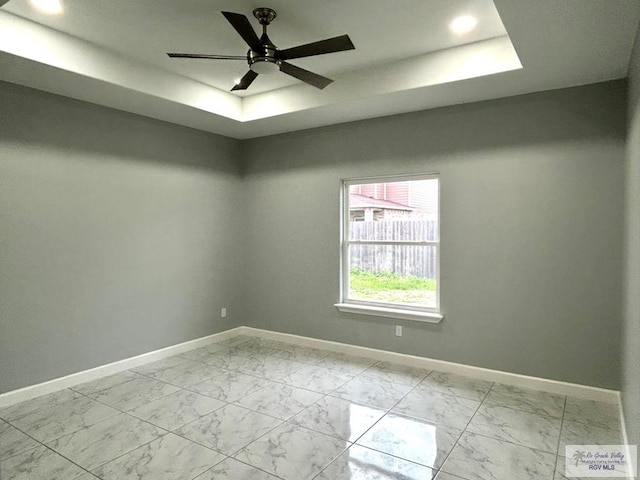 unfurnished room featuring a raised ceiling, light marble finish floors, baseboards, and a ceiling fan