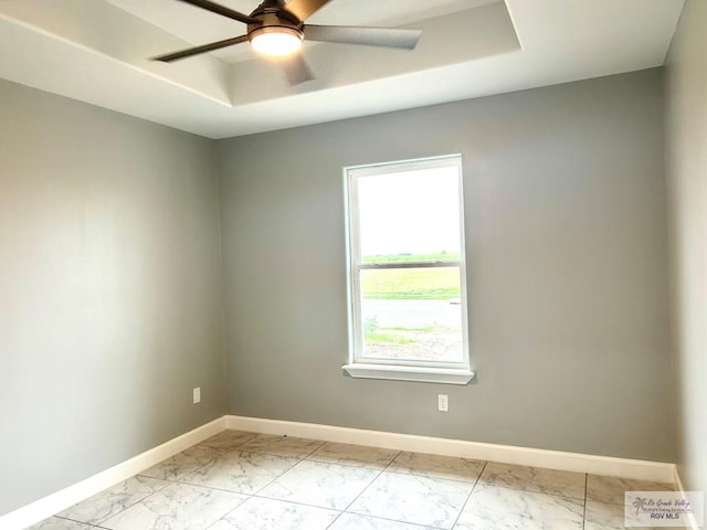 unfurnished room featuring light marble finish floors, baseboards, a ceiling fan, and a raised ceiling