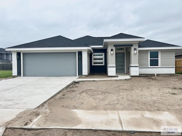 prairie-style house with a shingled roof, a garage, concrete driveway, stucco siding, and fence