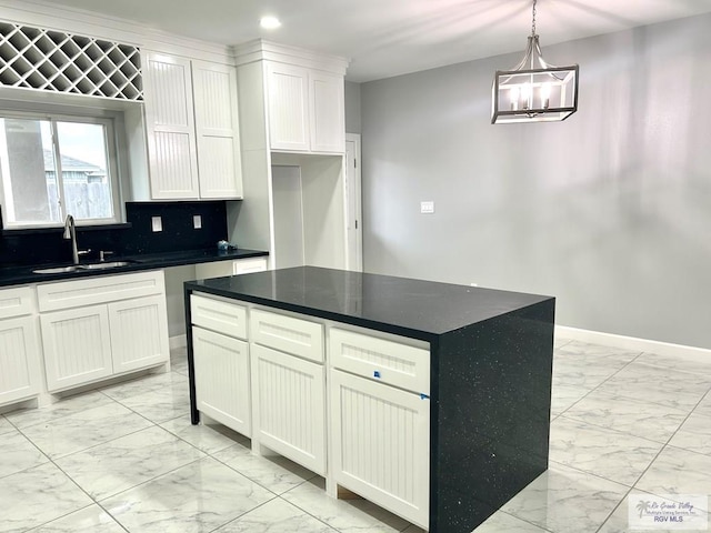 kitchen featuring a sink, light marble finish floors, dark countertops, white cabinets, and a chandelier