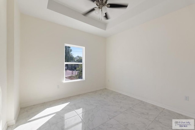 unfurnished room featuring marble finish floor, baseboards, a tray ceiling, and a ceiling fan