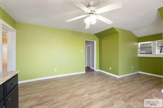 empty room featuring a textured ceiling, ceiling fan, vaulted ceiling, and light wood-type flooring