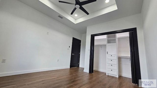 unfurnished bedroom with a tray ceiling, a closet, ceiling fan, and dark hardwood / wood-style flooring