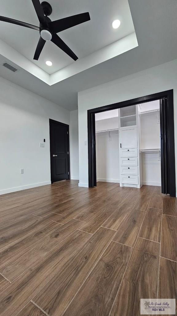 unfurnished bedroom with a tray ceiling, a closet, ceiling fan, and hardwood / wood-style floors