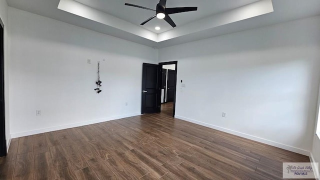 spare room featuring a tray ceiling, ceiling fan, and dark wood-type flooring