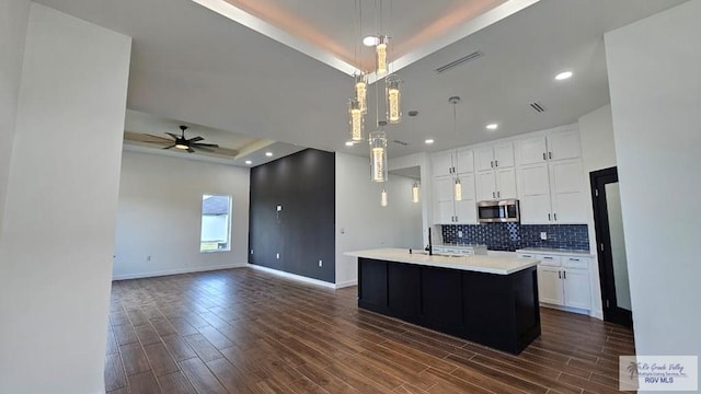 kitchen featuring a center island with sink, a tray ceiling, decorative light fixtures, dark hardwood / wood-style flooring, and white cabinetry