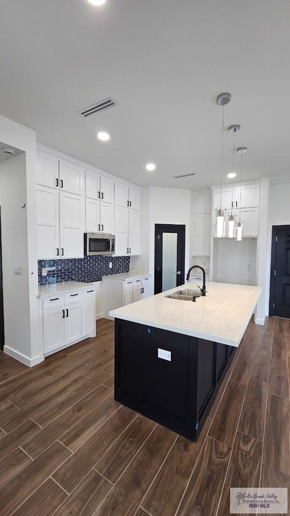 kitchen featuring dark wood-type flooring, white cabinets, a center island with sink, sink, and hanging light fixtures